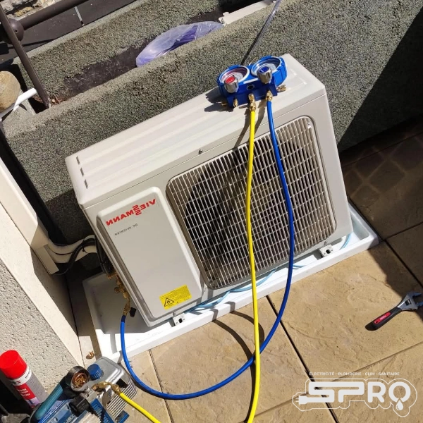 Unité de climatisation disposé à l'extérieur, sur le sol. Des cables sont posés dessus pour régler l'appareil et des outils sont visibles sur le côté bas gauche de l'image.