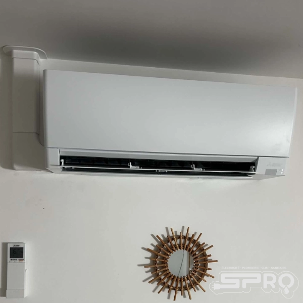 Climatisation à quelques centimètre du plafond, les raccords sont fait par le haut, vers le toit. On trouve une télécommande sur le coin bas gauche de l'image, ainsi qu'un miroir vers le centre.