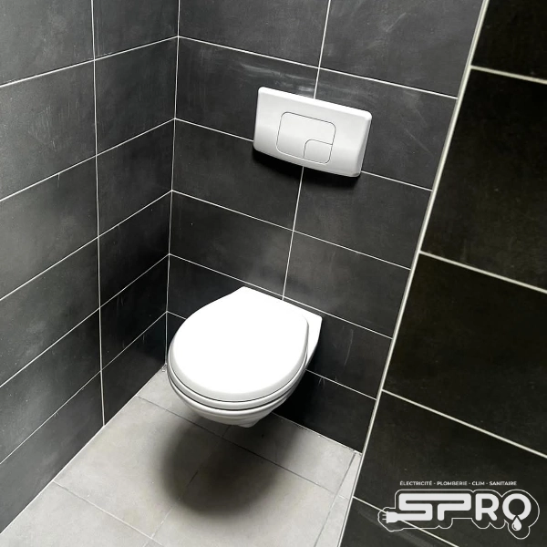 Toilette suspendu au mur, celui-ci a un carrelage de couleur noire avec des joints blanc. Le carrelage du sol est blanc. L'enclenchement de la chasse d'eau se trouve un dessus, encastré au mur.